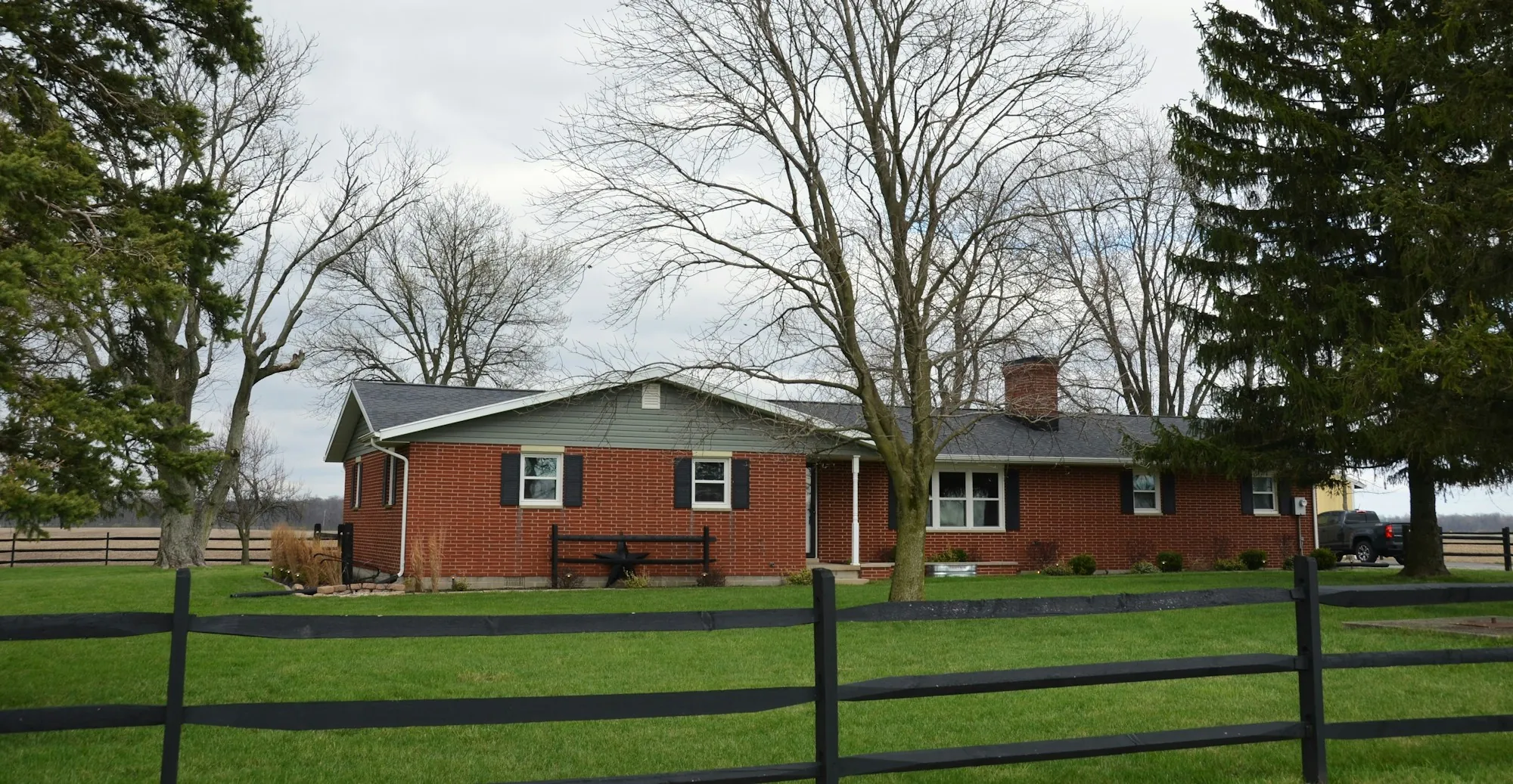 Long brick ranch home behind a wooden split-rail fence