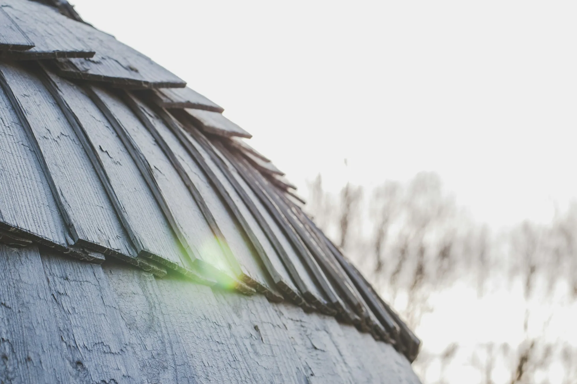 Curved edge of a wood shingle roof against a bright sky