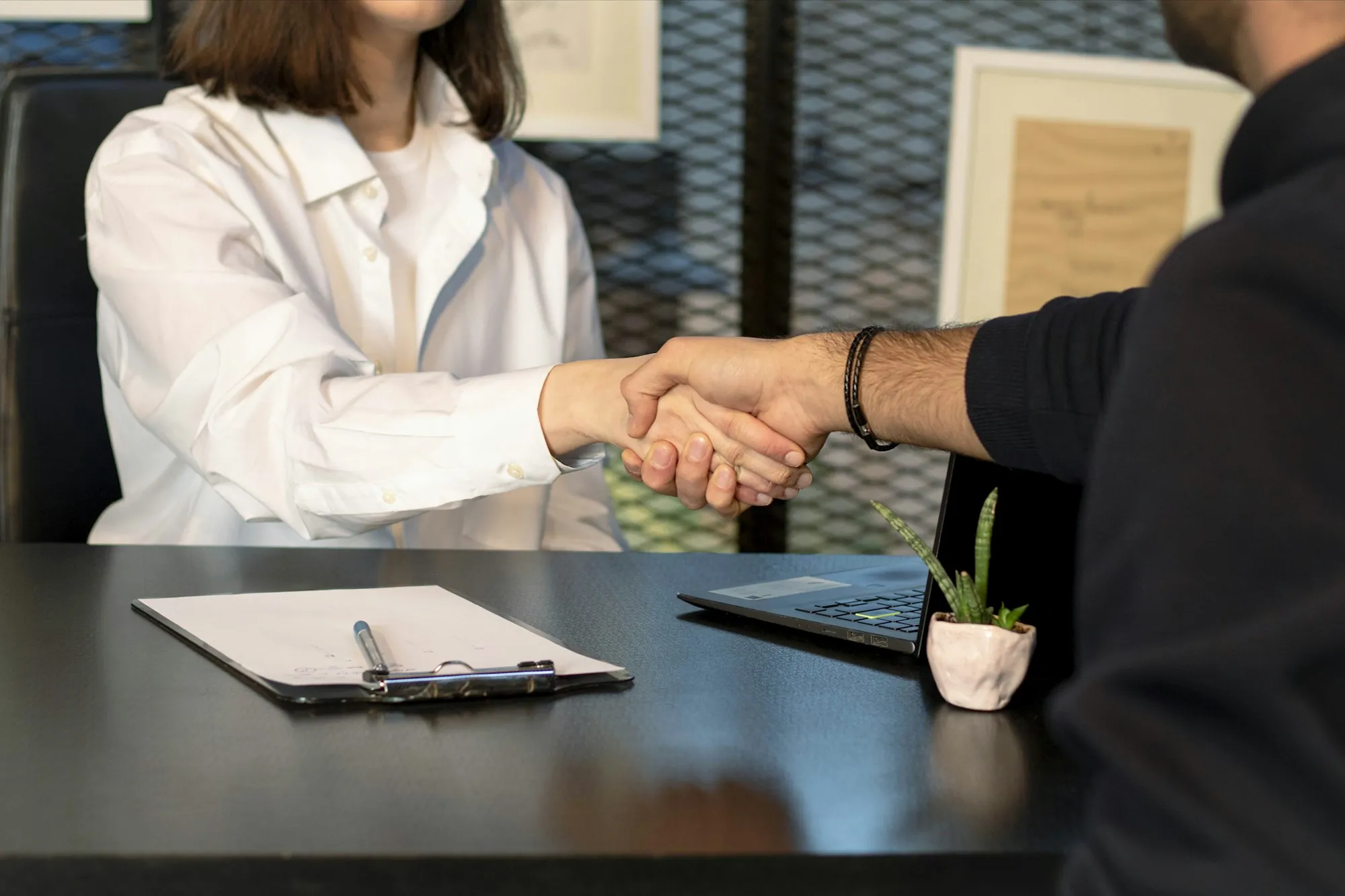 Handshake over a desk with a clipboard and paperwork
